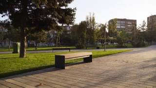 公园草坪上的现代木凳。时尚的新长椅在城市休闲区日出或日落。城市主义主题公共空间景观设计。空旷的街道人行道上没有人视频素材模板下载