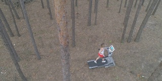 空中镜头。一名年轻女子在森林里的跑步机上跑步。