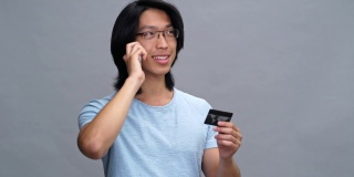 英俊开朗的年轻亚洲男子持有信用卡和电话交谈