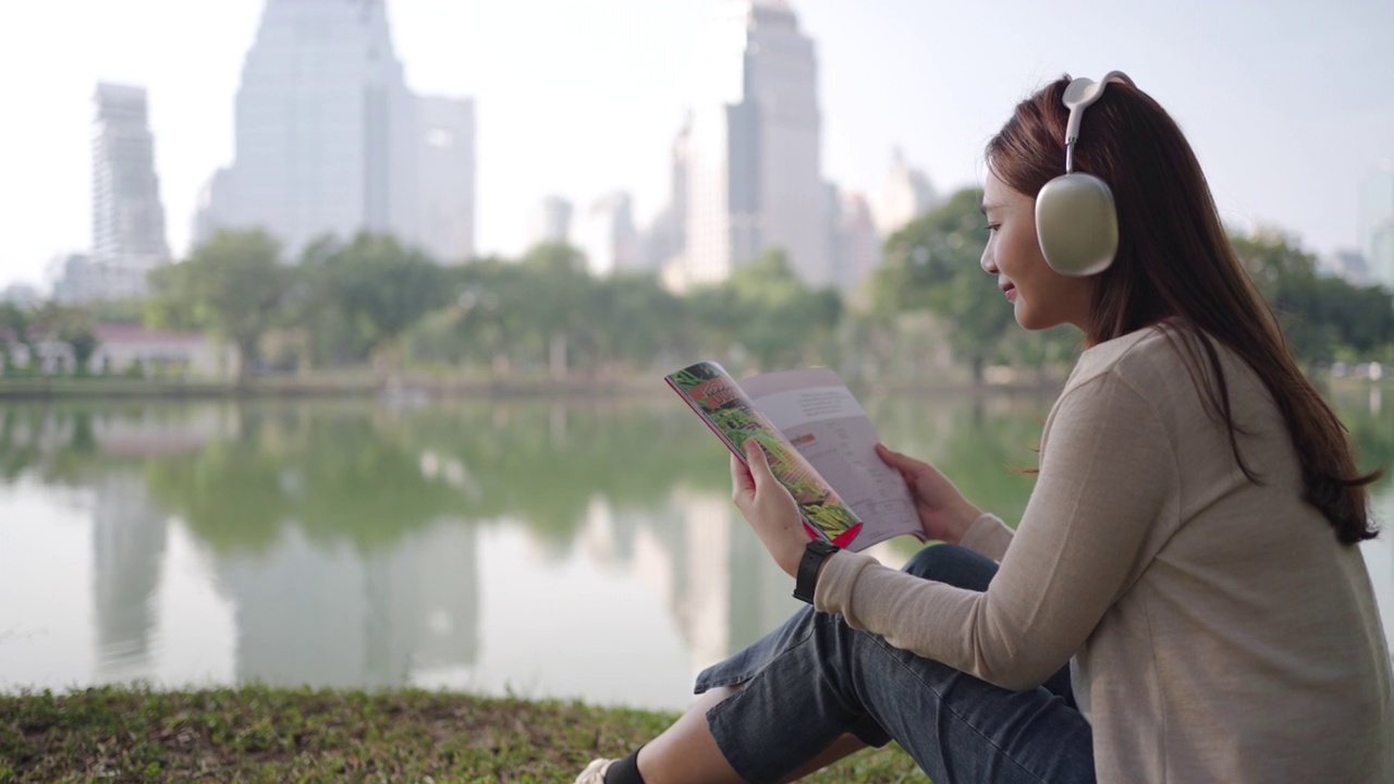 亚洲女人喜欢在早晨在城市公园听音乐和看书，人们在城市的自然环境中放松。