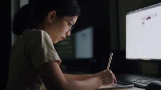 一名年轻女性晚上在家庭办公室用平板电脑写文章，滚动新闻推送，为她的工作计划搜索在线信息数据。视频素材模板下载