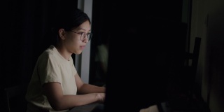亚裔自由职业女性，戴着眼镜，在电脑上打字，在社交媒体上阅读新闻。
