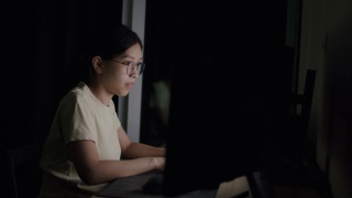 亚裔自由职业女性，戴着眼镜，在电脑上打字，在社交媒体上阅读新闻。视频素材模板下载