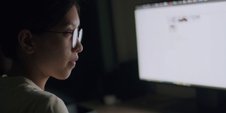 亚洲女性戴着眼镜，利用电脑搜索网上信息，为晚上的工作计划做准备。