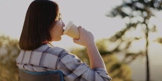 清晨，女人在户外的山上拿着咖啡杯放松