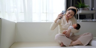 美丽的妈妈抱着可爱的新生儿用手机视频通话。技术