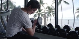 图为，一名亚洲男子上午在度假村健身中心进行哑铃重量训练。