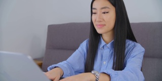 美丽的年轻亚洲妇女工作在笔记本电脑在4k股票视频。可爱的越南女孩，20多岁，在封锁期间在家用笔记本电脑做远程自由职业