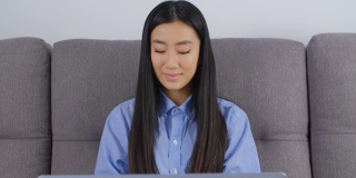 年轻的亚洲女性在家里用笔记本电脑工作。4k股票视频可爱的越南女孩在线学习。自由职业者女性做远程工作的笔记本电脑与一个愉快的微笑