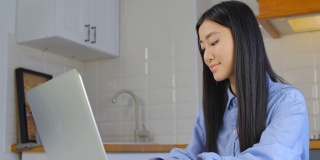 年轻漂亮的亚洲女人在笔记本电脑上工作。4k拍摄的远程学习概念。可爱的越南女孩在笔记本电脑上打字。自由职业女性在禁闭期间在家工作