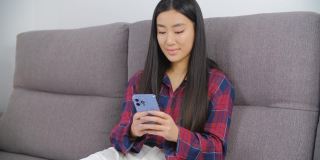 年轻的亚洲女性使用现代智能手机。美丽的越南女孩浏览社交媒体和互联网新闻feed在手机上与愉快的微笑。可爱的越南女性在网上交流