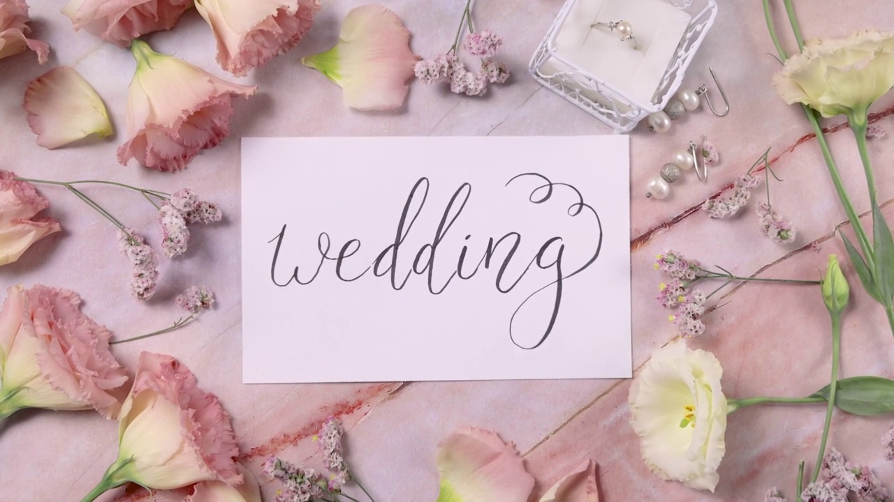 一张大理石桌子上的婚礼卡片，旁边是粉红色的花朵，俯视图放大