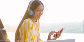 有吸引力的中国女性使用无线耳机和智能手机，快乐脸女人听喜欢的歌曲，跳舞，唱歌在舒适的阳光透过女人的背面。幸福的时刻