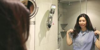 亚洲女人看着镜子。自信的亚洲女人做发型在浴室，准备在早上，享受每天例行公事。