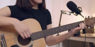 美丽的亚洲女人学习弹吉他和唱歌在家工作室。