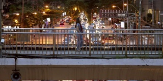 晚上，亚洲女性在城市繁忙的天桥上手持智能手机行走。