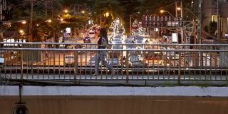亚洲妇女拿着智能手机在人行天桥上快速行走。在一个大都市的夜晚，城市交通模糊。