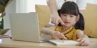 亚洲年轻妈妈用电脑笔记本教孩子在家学习或在线学习，在家在线教育的概念