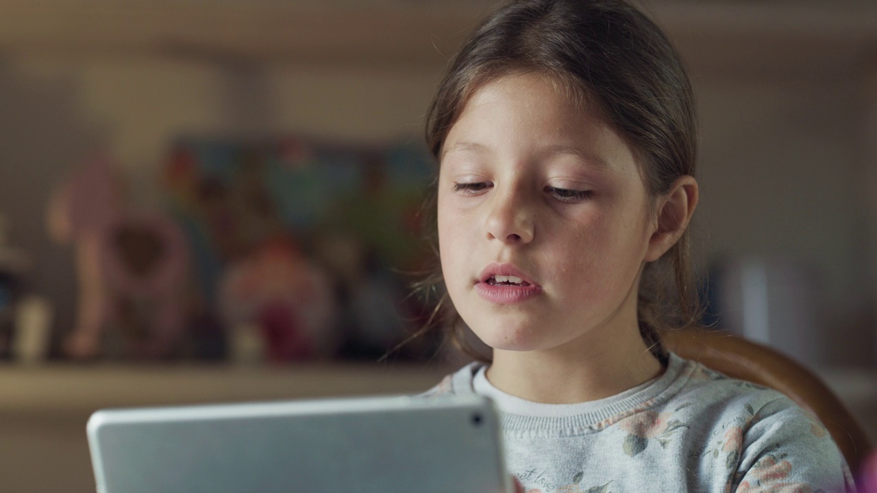 一个快乐的小女孩的真实照片是在她的房间里用平板电脑与朋友或亲戚进行有趣的自拍或技术视频通话。理念:技术、家庭、联系、新一代