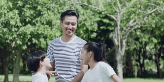 一位亚裔父亲在公园里和孩子们玩的时候把他的儿子抱起来