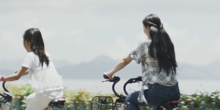 夏季，亚洲母女在海滨散步道上骑自行车