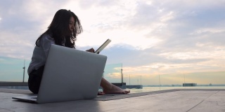 亚洲女商人完成了计算机工作。快乐轻松的女商人感觉压力减轻后工作做好。日落时分，游泳池边放松的女人在看平板电脑上的电影。