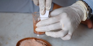 近距离拍摄的科学家的手戴着手套和混合的沙子样品和化学物质的土壤实验室测试。农业科学与实验