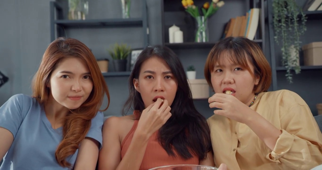 吸引人的亚洲可爱的女子组合尖叫震惊和恐惧时刻吃爆米花看恐怖网络电影娱乐在家里客厅的沙发上。周末生活方式活动隔离概念。