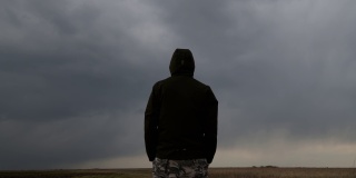 男性穿着连帽夹克的背影在天空中黑色的忧郁戏剧性的云