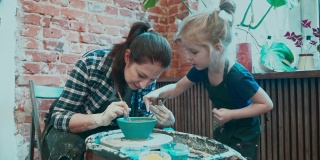 年轻的妈妈和她的小女儿在陶轮上学习陶艺，在现成的碗上画画。