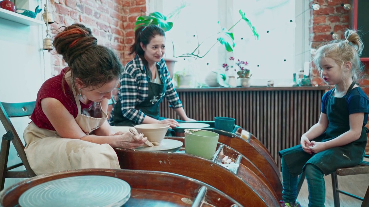一名年轻的教师正在教母亲和她的小女儿如何在作坊里用陶轮制陶。