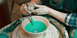 一个年轻女人的手用陶轮做陶器，在现成的碗上涂上釉。
