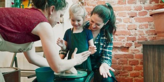 一名年轻的教师正在教母亲和她的小女儿如何在作坊里用陶轮制陶。