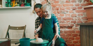 年轻的妈妈和她的小女儿在陶轮上学习陶艺，启动陶轮。