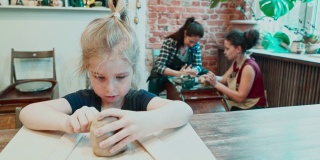 漂亮的小女孩正在用黏土雕刻，而她的妈妈正在一位年轻的女师傅的指导下制作陶器。