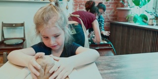 漂亮的小女孩正在用黏土雕刻，而她的妈妈正在一位年轻的女师傅的指导下制作陶器。