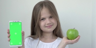 小女孩用绿色屏幕展示苹果和手机模拟手机、手机、手机。绿屏智能手机的色度键用于广告。水果、健康饮食、儿童口腔保健