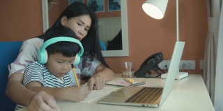 亚洲母亲教和解释家庭作业的孩子在线学习期间在家教育，概念在线学习