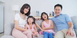 亚洲幸福家庭的肖像，花时间与孩子一起在家里。年轻可爱的小女孩和父母坐在沙发上微笑，看着客厅里的镜头。活动关系的概念