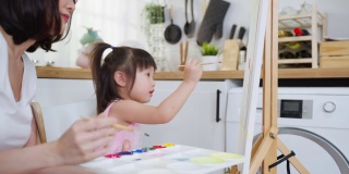 亚洲年轻快乐的女儿和妈妈在画板上画画。快乐的家庭活动，小女孩学习如何用水彩画和画笔画画，享受与妈妈的创造力。