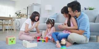 亚洲幸福家庭坐在地板上，在客厅里一起玩玩具。漂亮的父母和父母花时间和年轻的小女孩在家里。家庭活动关系概念。