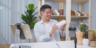 亚洲帅哥在家在线直播卖花瓶产品。年轻的商业男性用手提电脑向顾客展示商品并介绍细节。远程购买和购买购物概念。