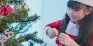亚洲年轻快乐的女孩孩子戴着圣诞帽，装饰圣诞树。小可爱的孩子穿着红布感到兴奋庆祝节日圣诞节感恩节派对在客厅在房子。