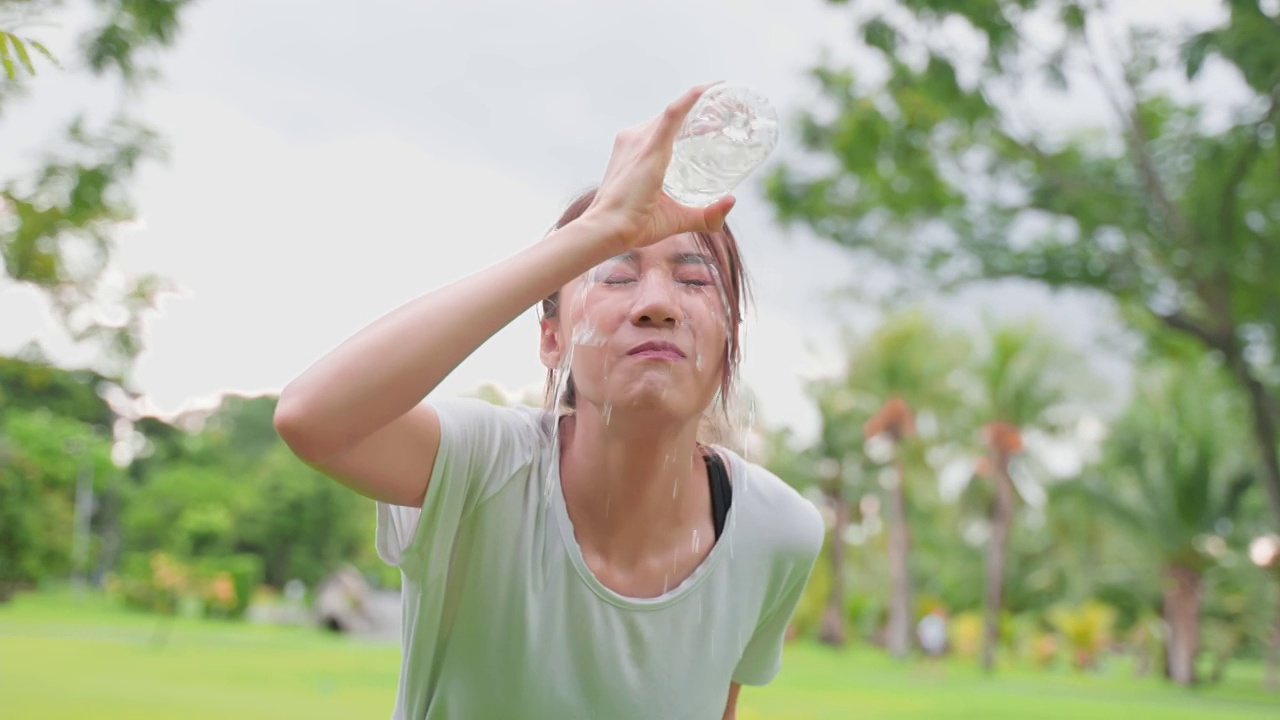 亚洲年轻女运动员在公园运动后喝瓶装水。活跃迷人美丽的女运动员，瑜伽后休息，晚上在户外跑步锻炼，在花园保健。