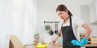 亚洲年轻清洁服务女工清洁厨房桌子在家里。年轻的女管家清洁工感到沮丧，而擦拭脏乱的烹饪柜台家务或杂务。