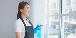 亚洲清洁服务女工清洁客厅在家里。美丽的主妇管家清洁工穿着围裙，擦拭着清洗脏乱肮脏的玻璃窗，负责家务劳动或杂务
