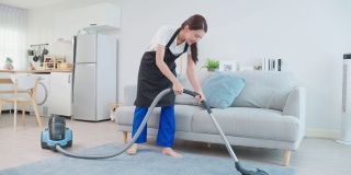 亚洲清洁服务女工清洁客厅在家里。美丽的年轻女孩管家清洁工穿围裙和吸尘肮脏的地板，家务和家务在房子。