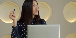 富有思想的商业亚洲妇女在电脑前工作，微笑着看着远方，想着一个成功的商业