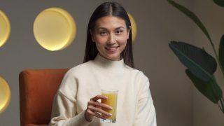 一位美丽的亚洲女子手里拿着一杯橙汁，看着镜头视频素材模板下载