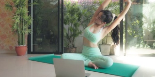 年轻的亚洲妇女在家里玩瑜伽在线健康或健康的生活方式。